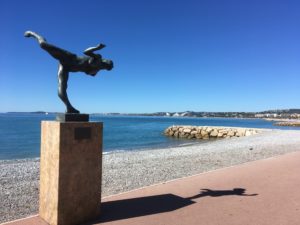 Statue en bronze représentant une muse en équilibre avec la mer et les plages de galet en fond 